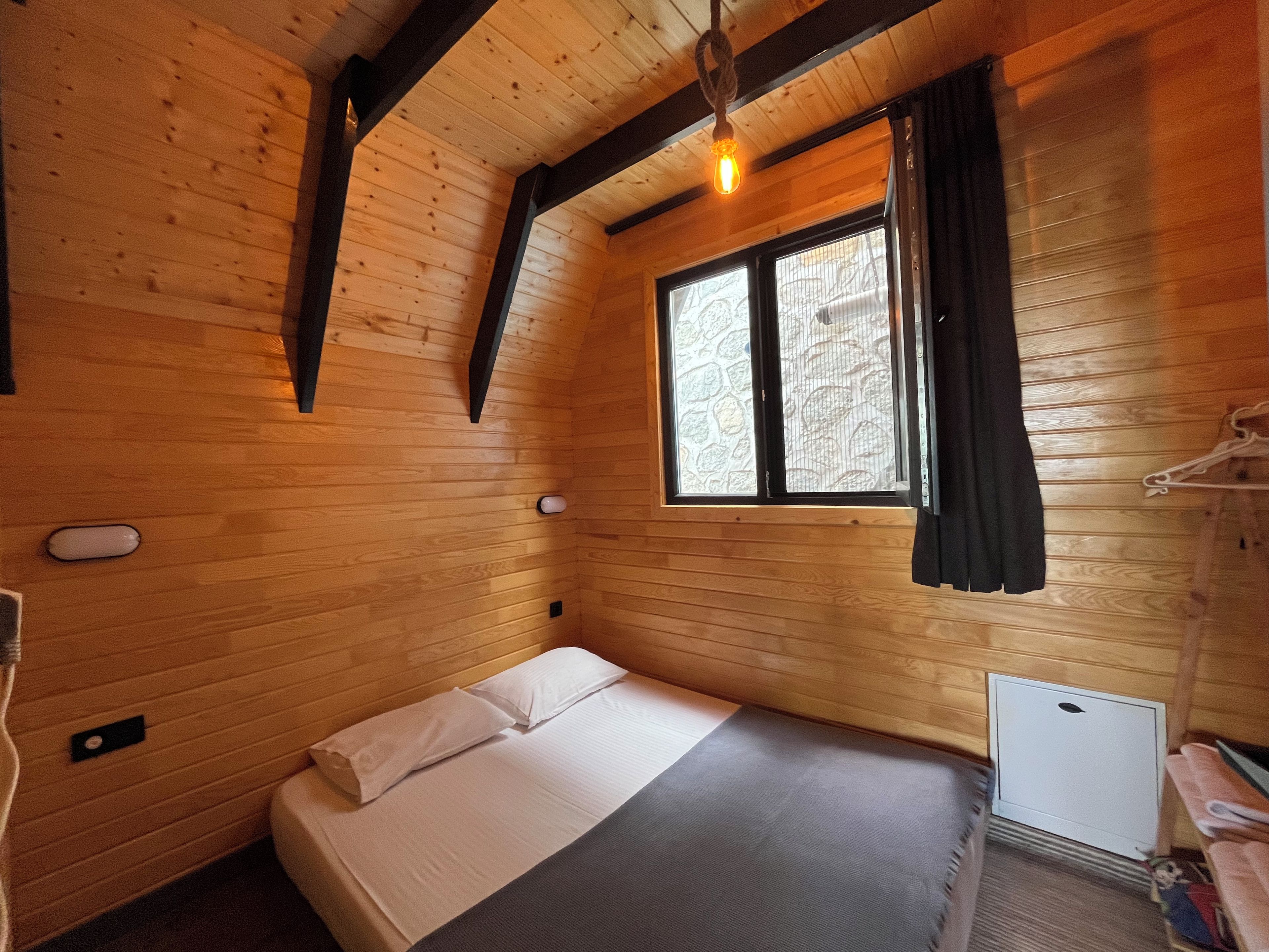 Una habitación de cabaña de madera con una cama, un ventanal y un pequeño radiador.