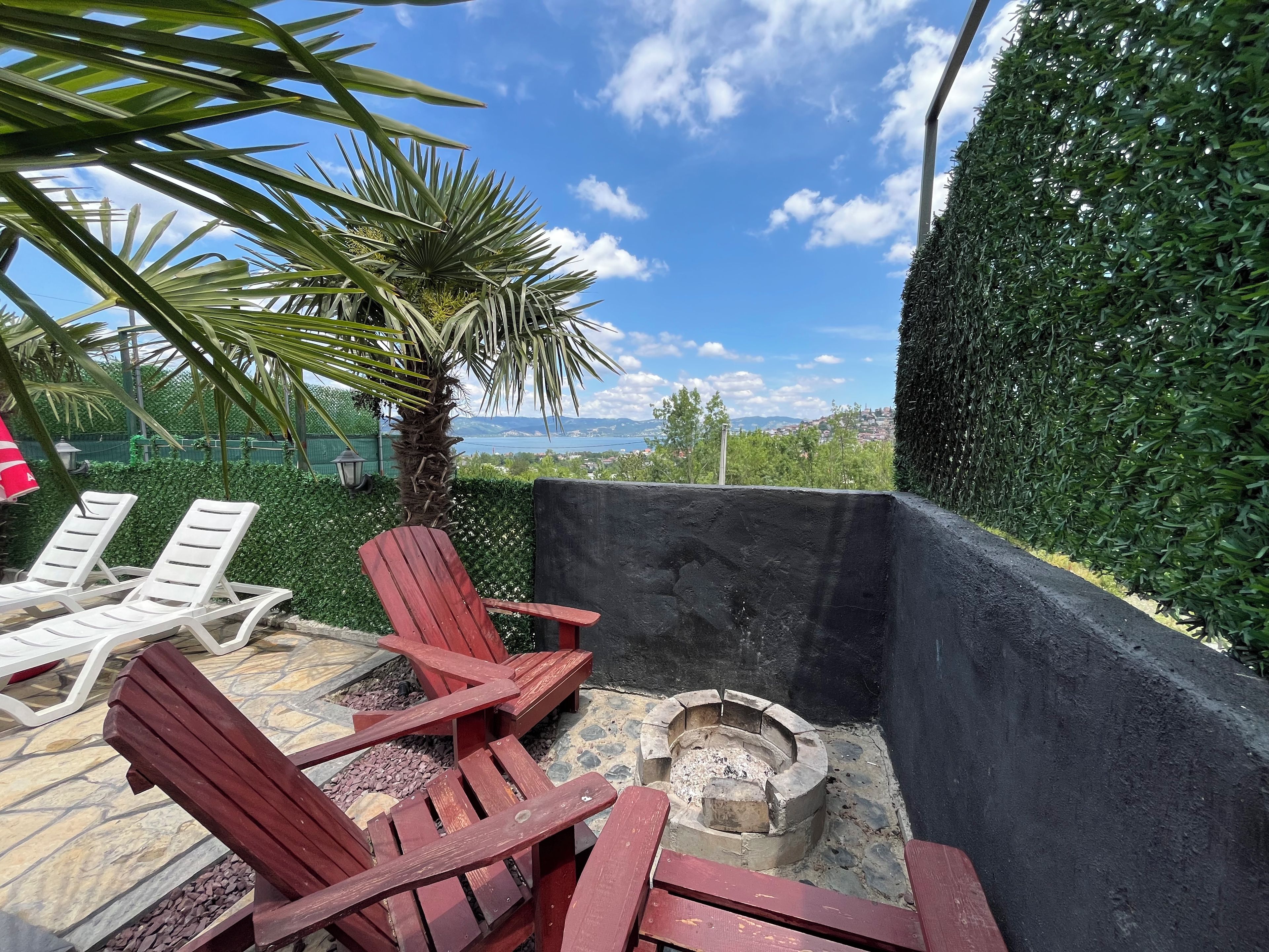 Un patio con dos sillones blancos, una silla roja y un hogar de piedra.