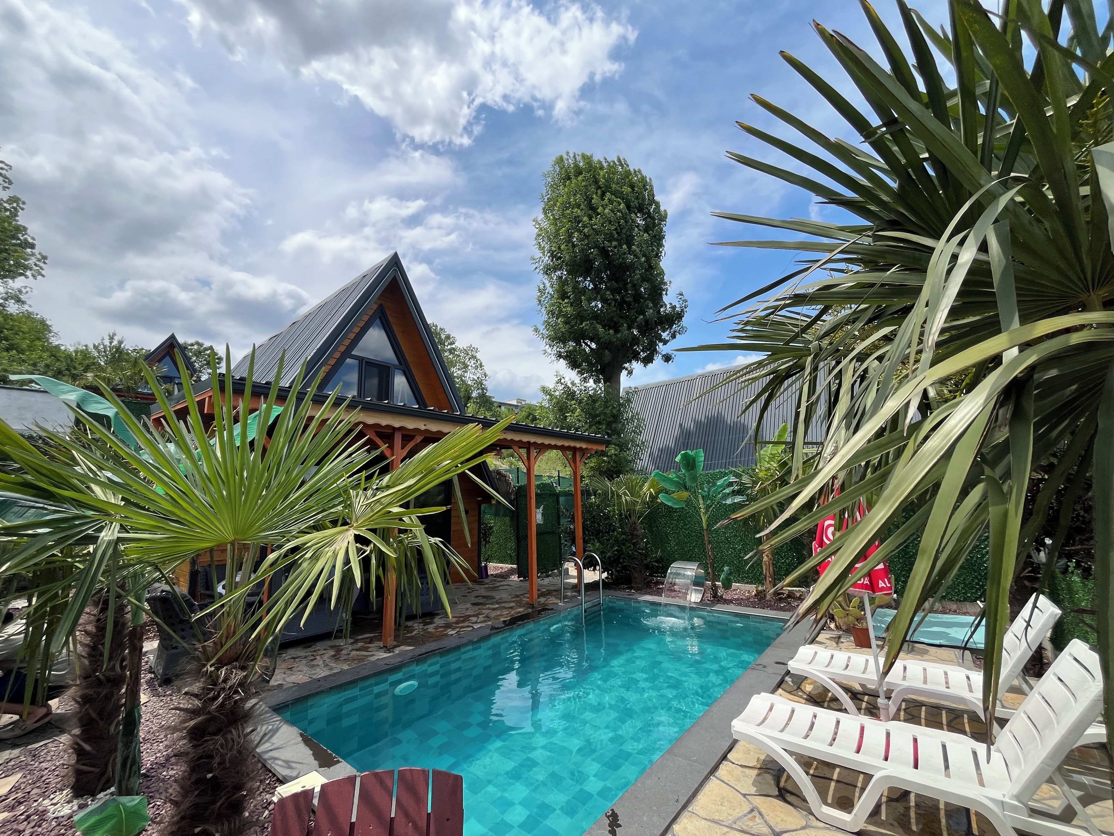 Una piscina con sillas de descanso, una casa de madera y plantas tropicales.