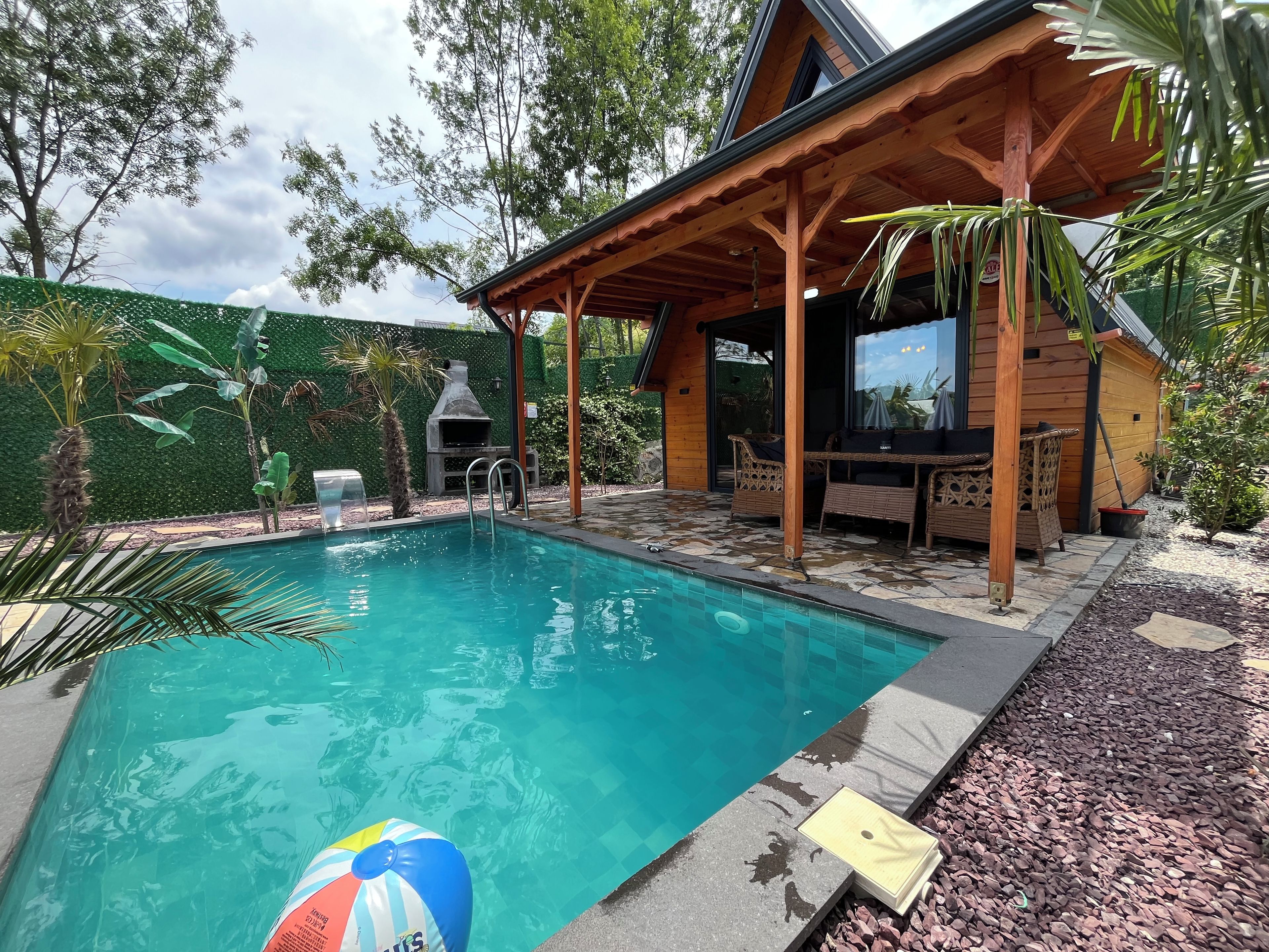 Una piscina con cubierta de madera, una parrilla y mobiliario de mimbre.