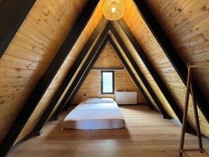 Una habitación con techo inclinado, paredes de madera, una cama, un radiador y una ventana.