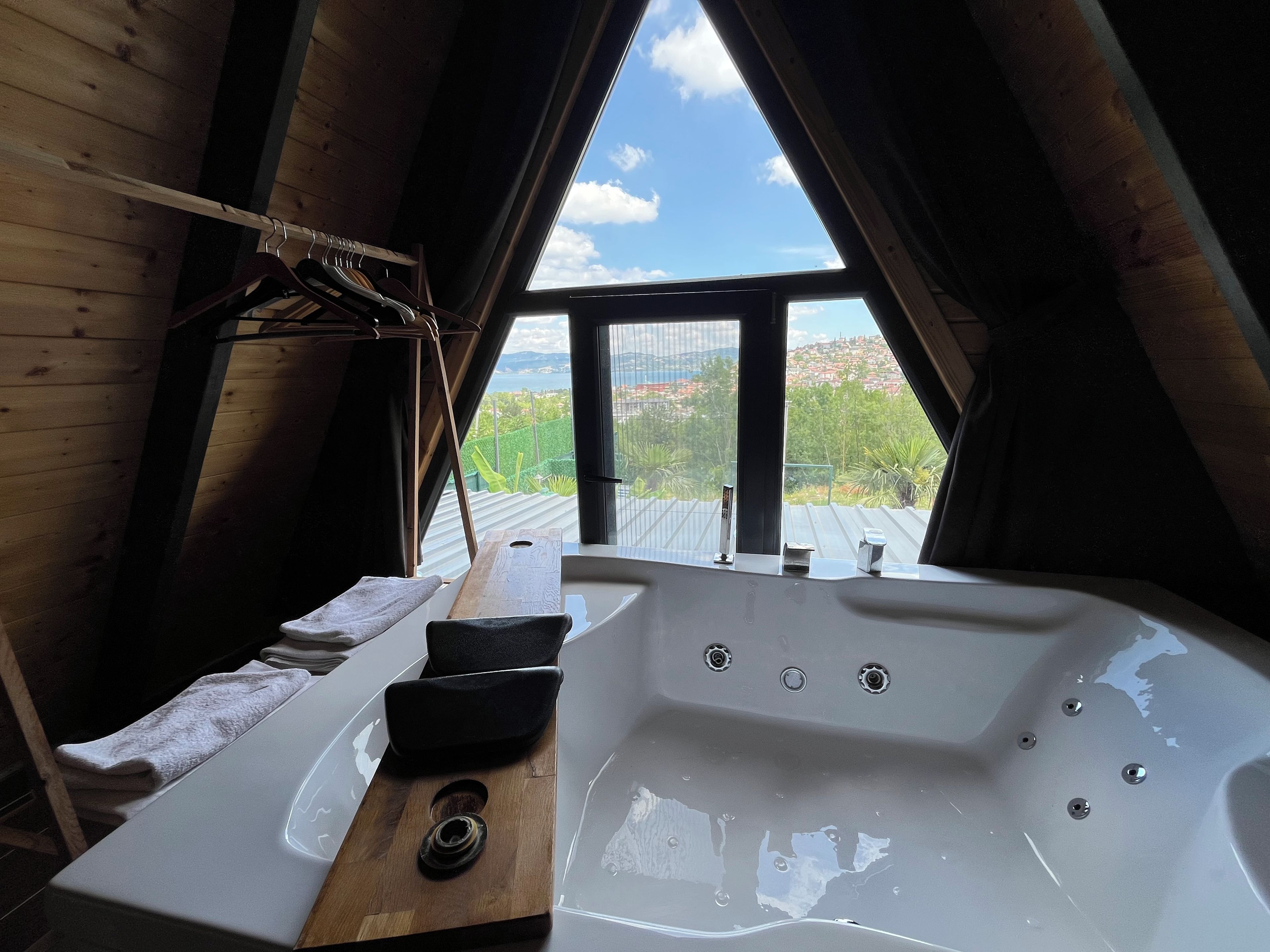 Un baño con bañera, banco de madera y vistas a un paisaje urbano a través de un ventanal grande.