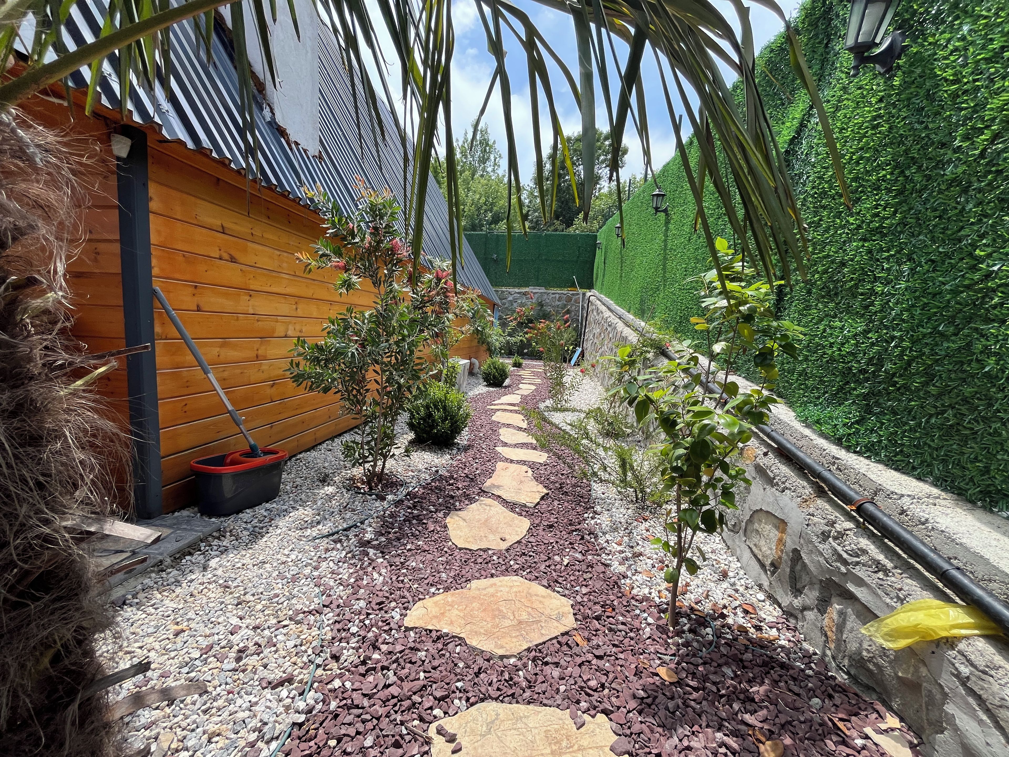 Un sendero en un jardín con piedras para pisar, una cerca de madera y un seto verde.