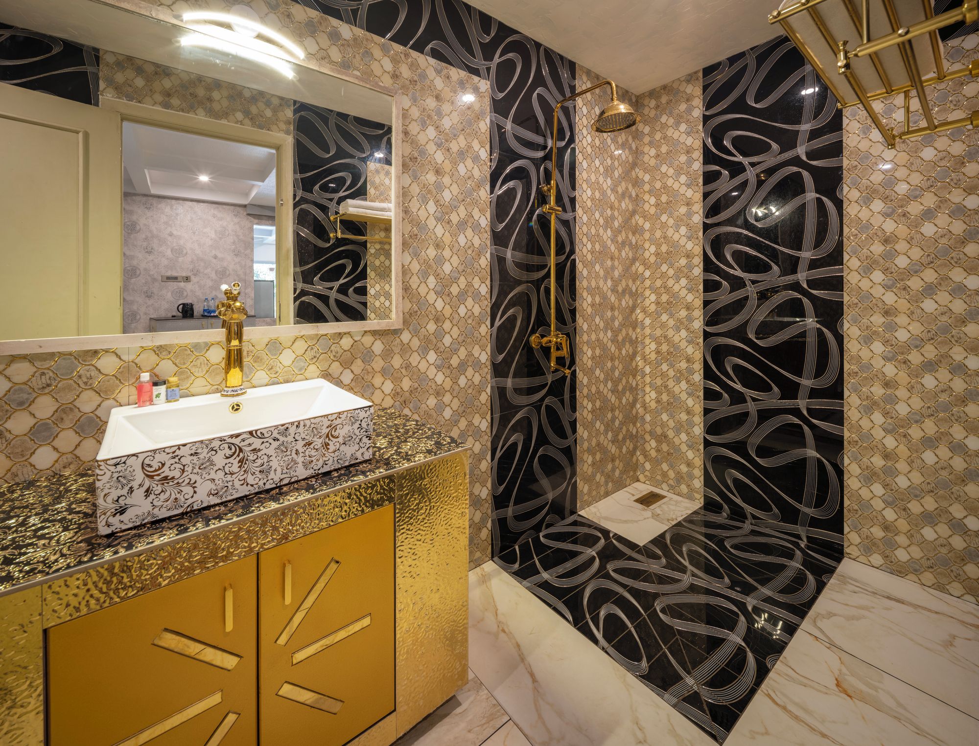 Un baño con tocador dorado, lavamanos blanco y ducha con diseño negro y dorado.