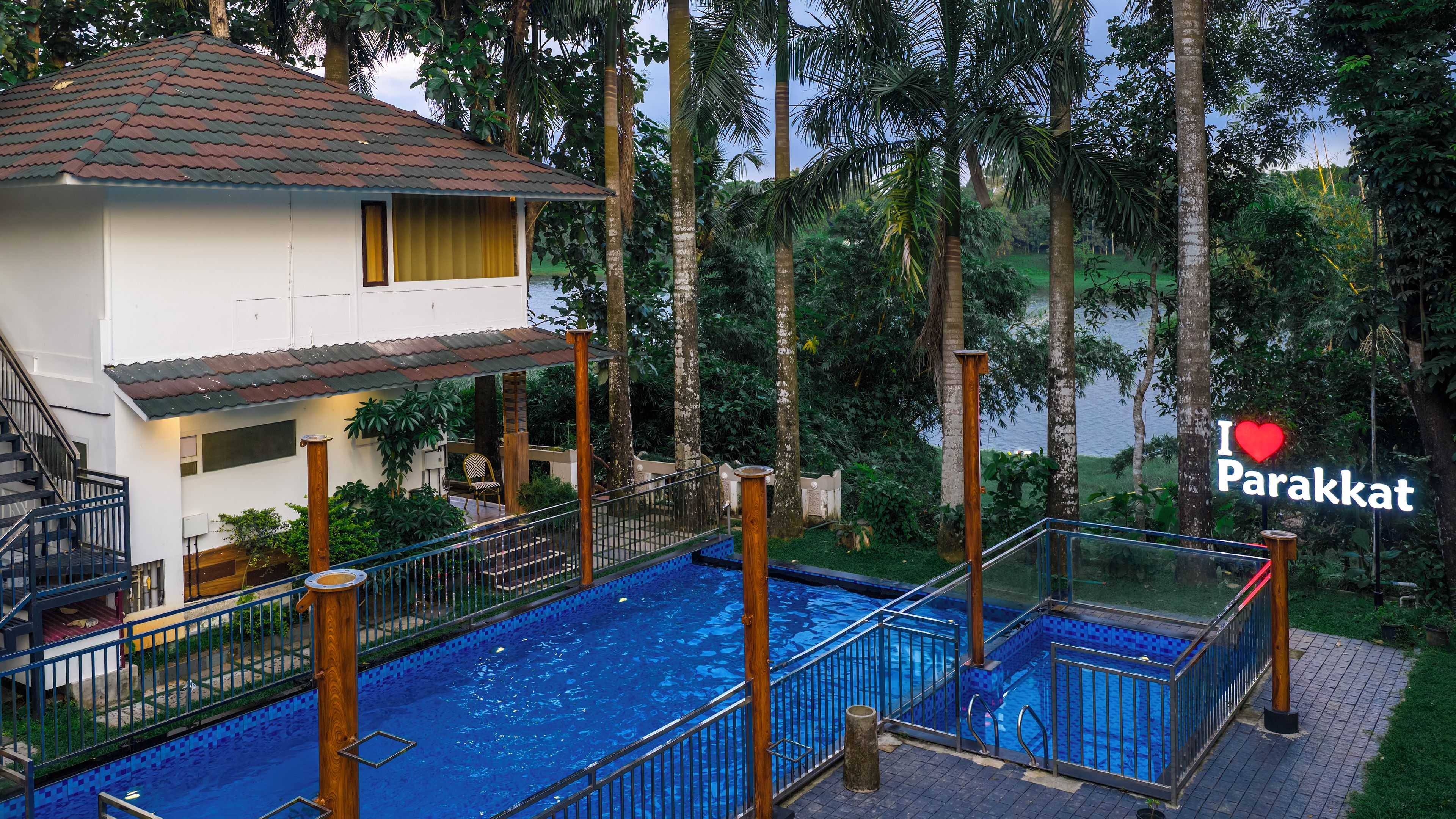 A two-story building with a swimming pool, surrounded by tropical vegetation.