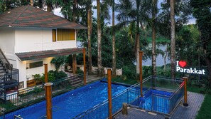 Un edificio de dos plantas con piscina, rodeado de vegetación tropical.