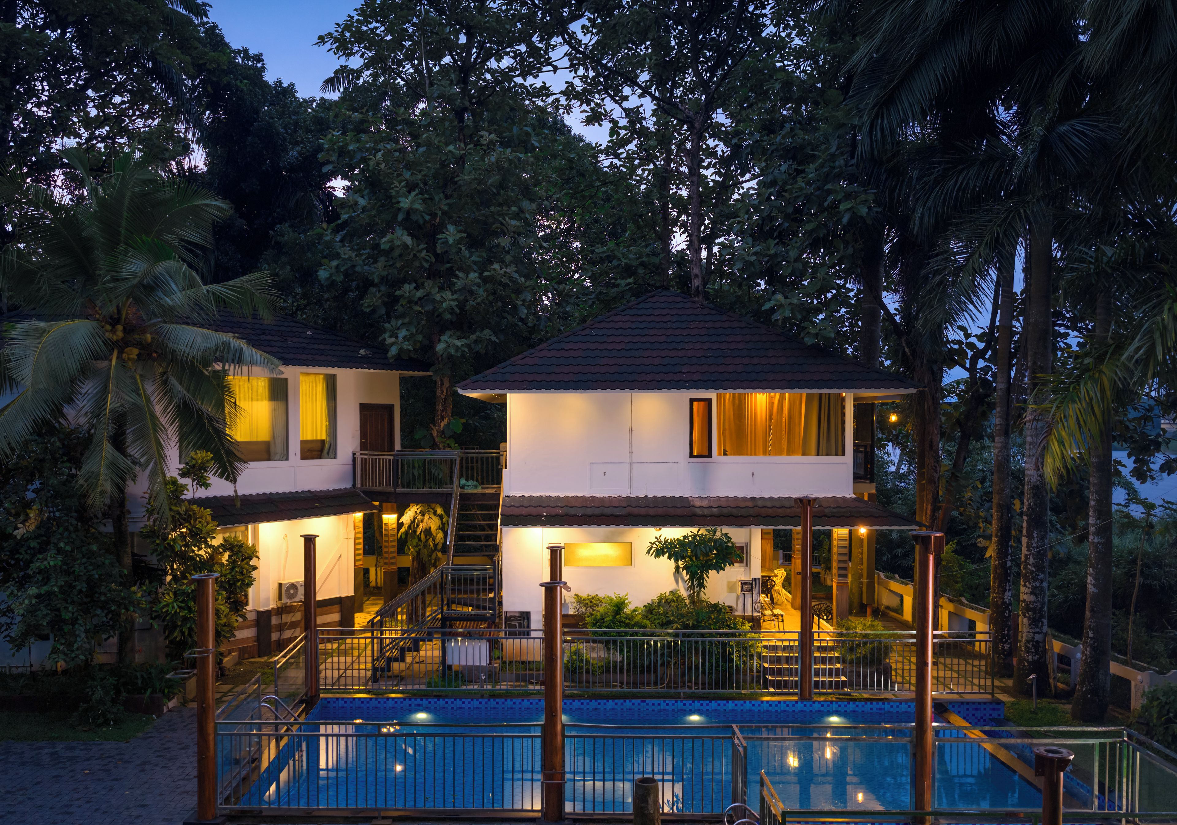 A two-story house with a swimming pool, surrounded by tropical vegetation.
