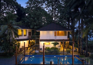 Una casa de dos pisos con piscina, rodeada de vegetación tropical.