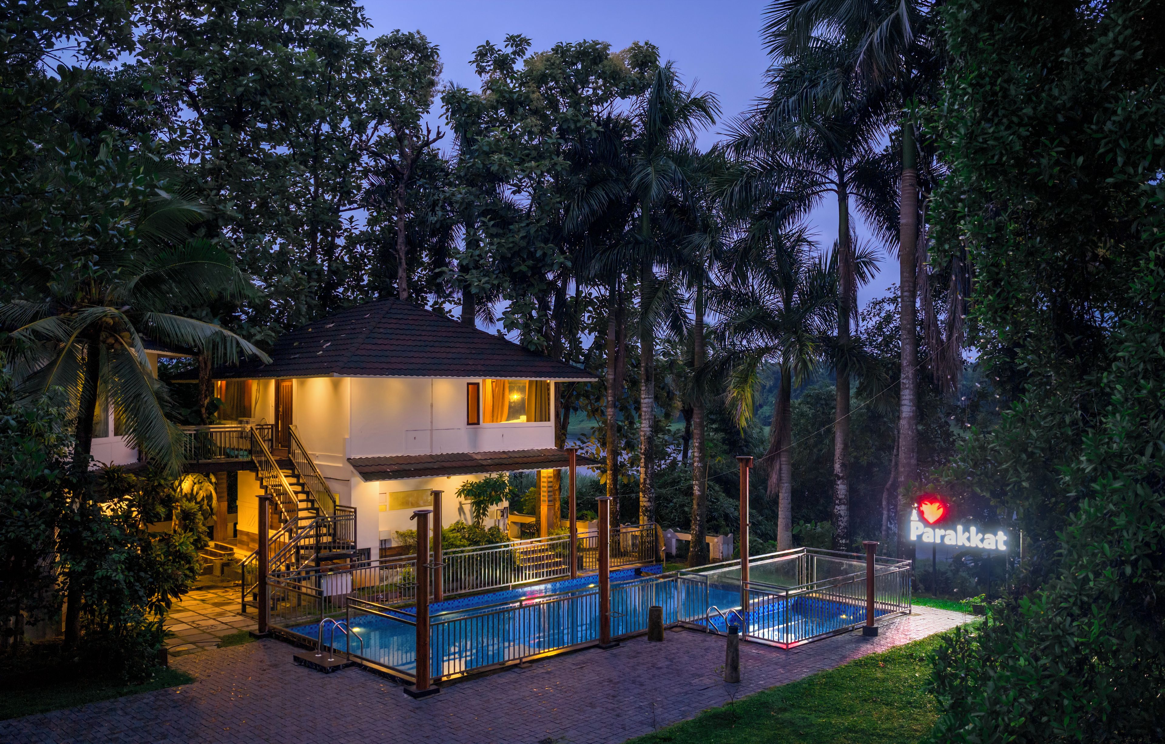 A two-story building with a swimming pool, surrounded by lush greenery and palm trees.