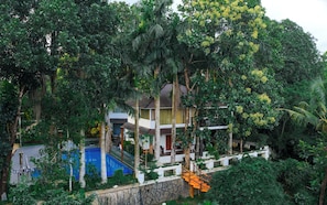 A two-story house surrounded by dense greenery, with a visible swimming pool and a stone wall. - Riverscape By Parakkat (Kunnathunad)