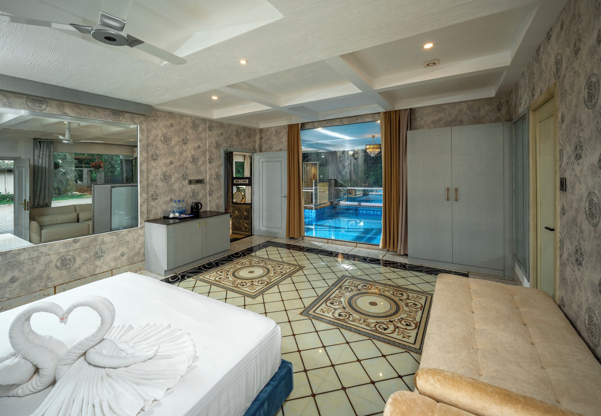 Habitación de hotel con una cama grande, zona de estar, vista a una piscina exterior y un espejo amplio.