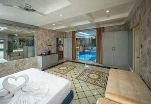 A hotel room with a large bed, a sitting area, a view of an outdoor swimming pool, and a large mirror. - Riverscape By Parakkat (Kunnathunad)