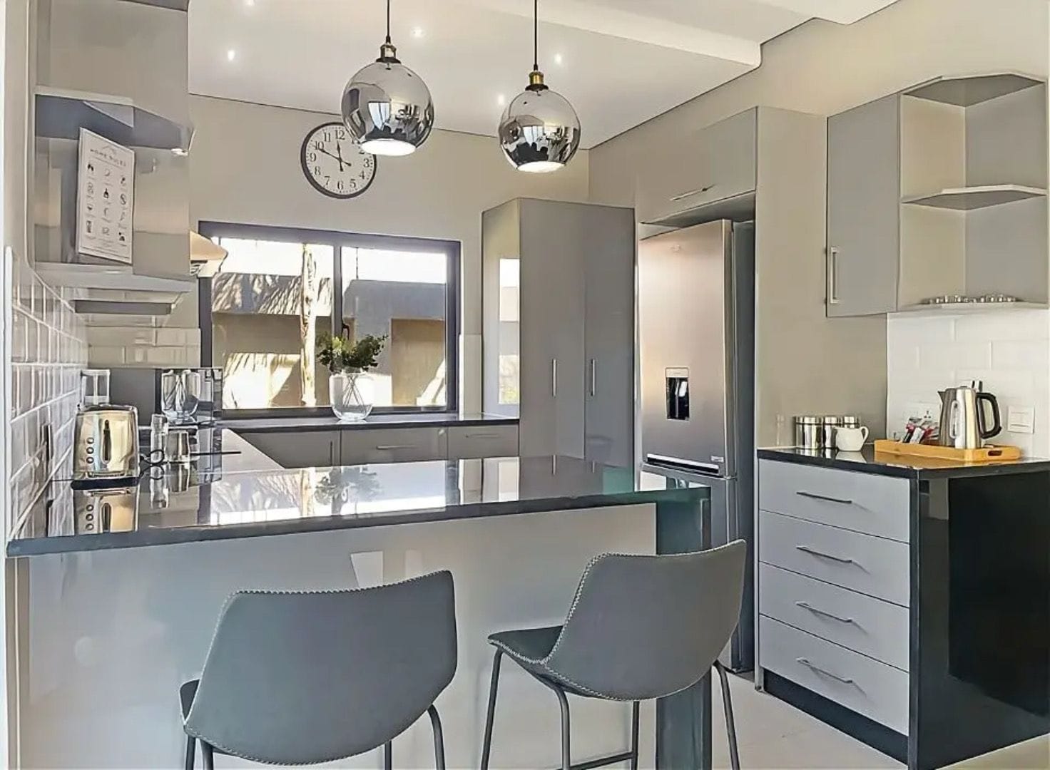 A modern kitchen with a central island, two chairs, stainless steel appliances, and pendant lighting.