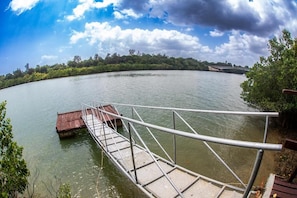 A metal bridge over calm water with a forested shoreline and a cloudy sky. - Mango Villa (Mtwapa)