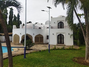 A white building with arched windows and a pool area. - Mango Villa (Mtwapa)