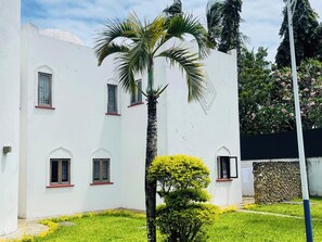 A white building with multiple windows and a palm tree in the foreground. - Mango Villa (Mtwapa)