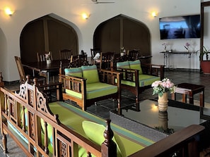A hotel lobby with traditional wooden furniture, a flat-screen TV mounted on the wall, and a potted plant on a side table. - Mango Villa (Mtwapa)