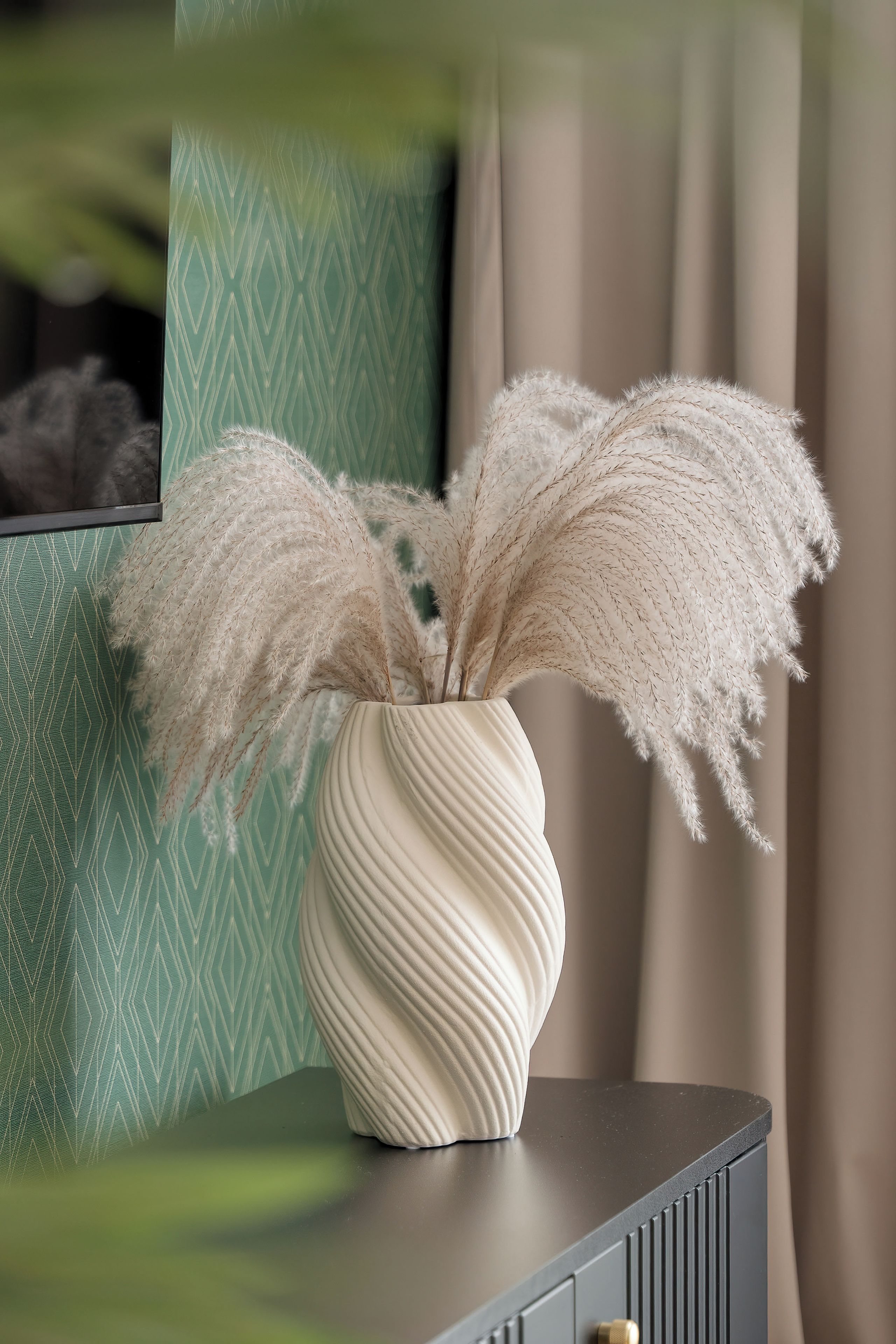 Un vase blanc orné de plumes d’herbe de la pampa, posé sur une surface sombre.