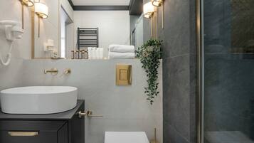 Ein modernes Badezimmer mit einem großen weißen Waschbecken, goldenen Armaturen, einem Handtuchhalter mit Handtüchern und einer Topfpflanze.