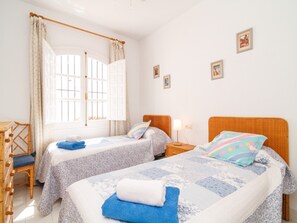 Ein Hotelzimmer mit zwei Betten, einem fensterbelaubten Fenster, einem Holzstuhl und einem kleinen Tisch.