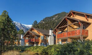 A row of wooden cabins with balconies, set against a backdrop of snow-capped mountains and dense forest. - Oktoberfest & Marathon Weekend! 2BR WorldMark Resort (Leavenworth)