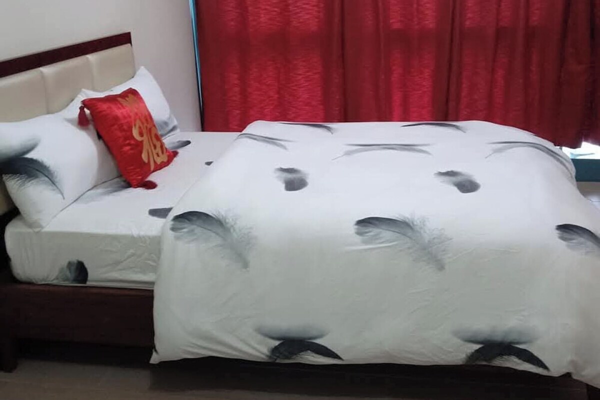 A bed with a white and grey patterned bedspread, a red pillow, and a wooden headboard.