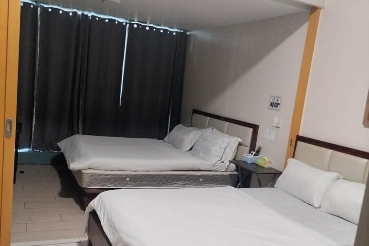 A hotel room with two beds, a nightstand, and a window with curtains.