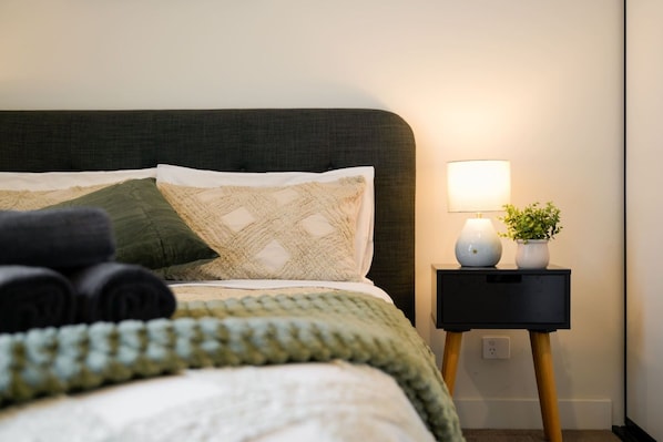 Un lit bien fait, avec des serviettes pliées, une lampe de chevet et une petite plante posée sur une table de chevet.