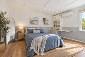 Ein Schlafzimmer mit einem Bett, Nachttischen, einem Spiegel, einem Fenster und einer Wand-Klimaanlage.