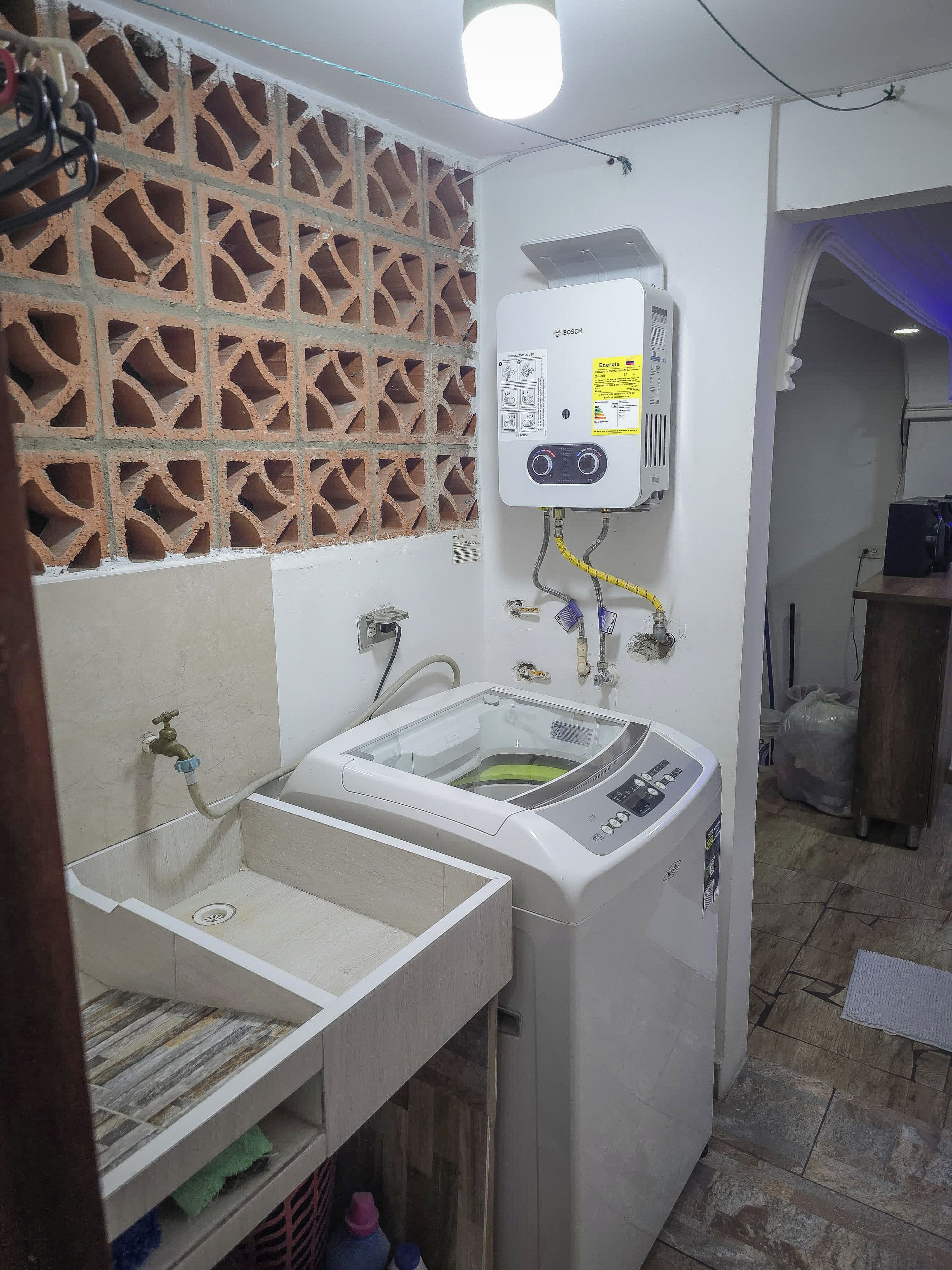 Ein kleiner Hauswirtschaftsraum mit einem Bosch-Warmwasserspeicher, einer Waschmaschine und einem Waschbecken.