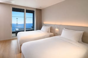 Een hotelkamer met twee bedden, een groot raam met uitzicht op zee en een schuifdeur.