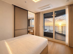 Habitación de hotel con cama, zona de estar con vista al mar y balcón con vistas al atardecer.