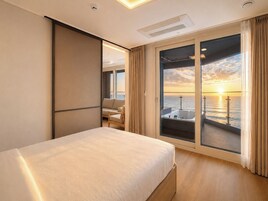 Habitación de hotel con cama, zona de estar con vista al mar y balcón con vistas al atardecer.
