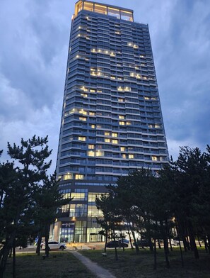 A tall, modern building with multiple floors and balconies, surrounded by trees and a parking area. - Emerson Suites Naksan (Yangyang)