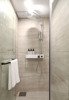 A modern shower with a handheld showerhead, a wall-mounted control panel, and a shelf with toiletries.
