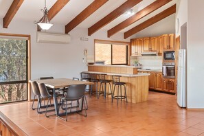 A kitchen with wooden cabinets, a central island with stools, and a dining area with a table and chairs.