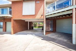 A two-story building with a covered parking area, a gated entrance, and a balcony with a view.