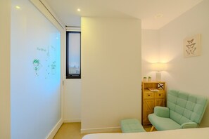 Un dormitorio con cama, mesita de noche, ventana y un cuadro de una mariposa en la pared.
