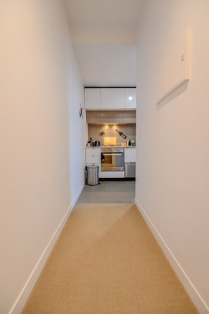 A narrow hallway leading to a kitchen with white cabinets, a stainless steel oven, and a trash bin. - Stay in the Heart of Melbourne CBD-Walk Everywhere (Melbourne)