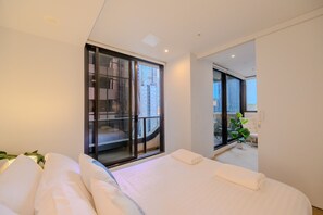 Habitación de hotel moderna con una cama grande, una puerta corrediza de cristal que da a un balcón y vistas a la ciudad.