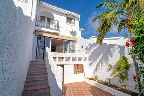 A white building with a balcony, steps leading to the entrance, and a small garden area with a palm tree. - Villa in Nerja Near Burriana Beach (Nerja)