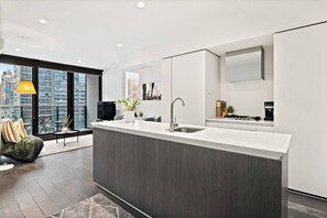 A modern kitchen with a large island, a built-in sink, and a dining area with a sofa and a table. - Elegant 2BR Apt | Panoramic Views • Pool & Gym (Melbourne)