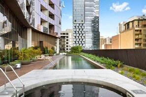 A rooftop pool area with a view of surrounding buildings, including a tall glass skyscraper. - Elegant 2BR Apt | Panoramic Views • Pool & Gym (Melbourne)