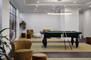 A modern indoor setting with a pool table, comfortable seating, and a large window providing natural light. - Cozy 2BR Apt | Vibrant Living w/ Pool & Gym (Melbourne)