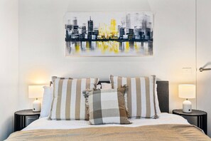 Ein Hotelzimmer mit Bett, gestreiften Kissen, zwei Nachttischlampen und einem Stadtbild an der Wand.