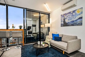 Ein modernes Wohnzimmer mit einer Couch, einem Couchtisch und Sesseln, einem großen Fenster mit Blick auf die Stadt und einem Gemälde an der Wand.