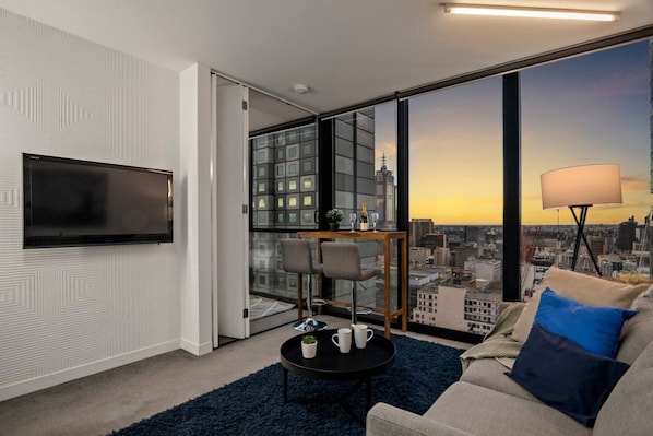 Een moderne woonkamer met uitzicht over de stad, een flatscreen televisie, een eettafel en een bank.