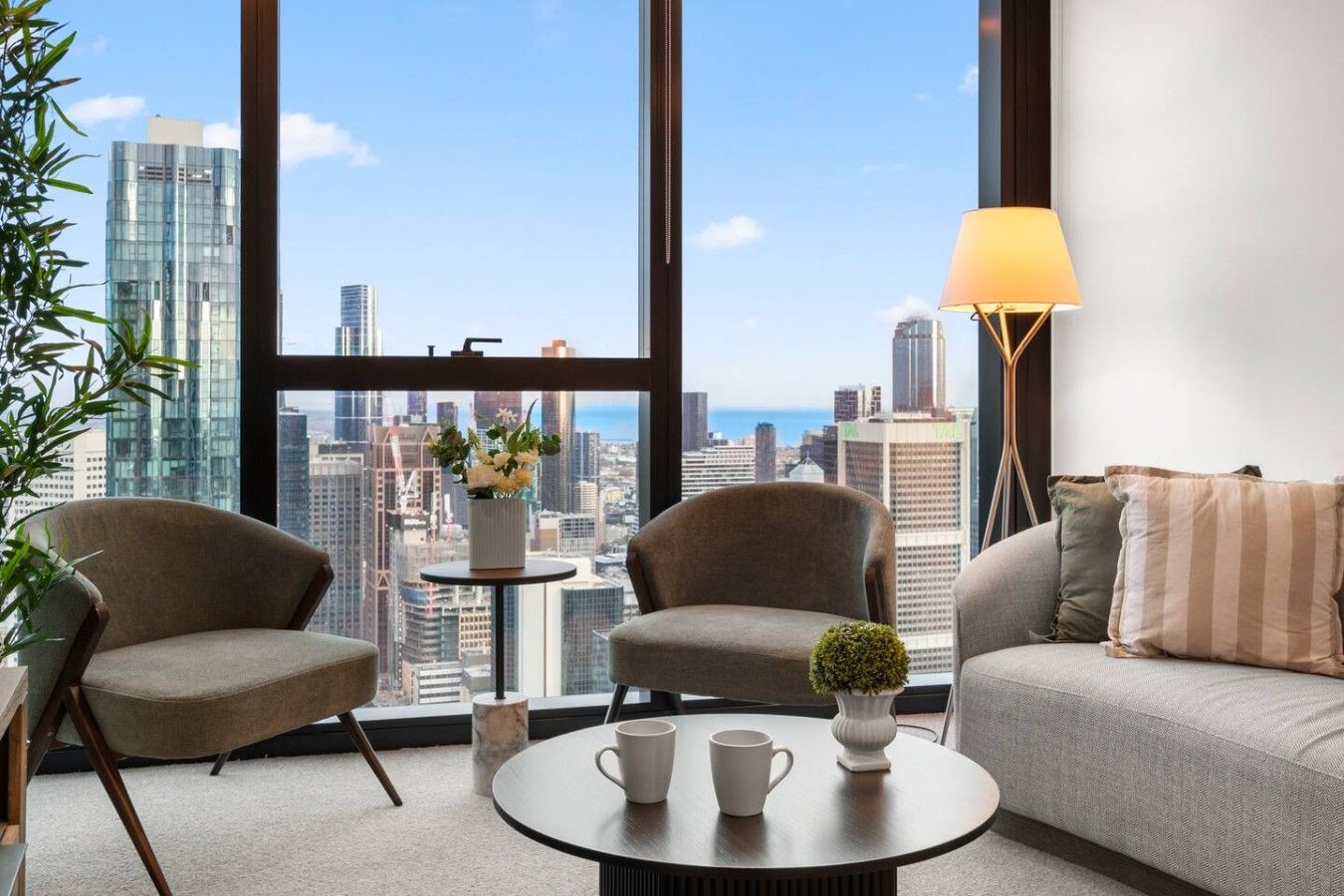 Uma sala de estar moderna com vista para a cidade, dois poltronas, um sofá, uma mesa de centro e um abajur.
