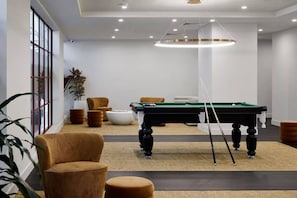 A modern indoor pool table with a green felt surface, surrounded by brown upholstered chairs and a white round table. - LVL 56 City Skyline | Stylish 3B Apt w/ Pool & Gym (Melbourne)