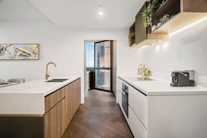 A modern kitchen with a central island, wooden cabinets, and a built-in oven. - LVL 56 City Skyline | Stylish 3B Apt w/ Pool & Gym (Melbourne)